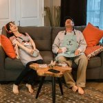 Tired married couple in home clothes sitting on the sofa with cups of tea